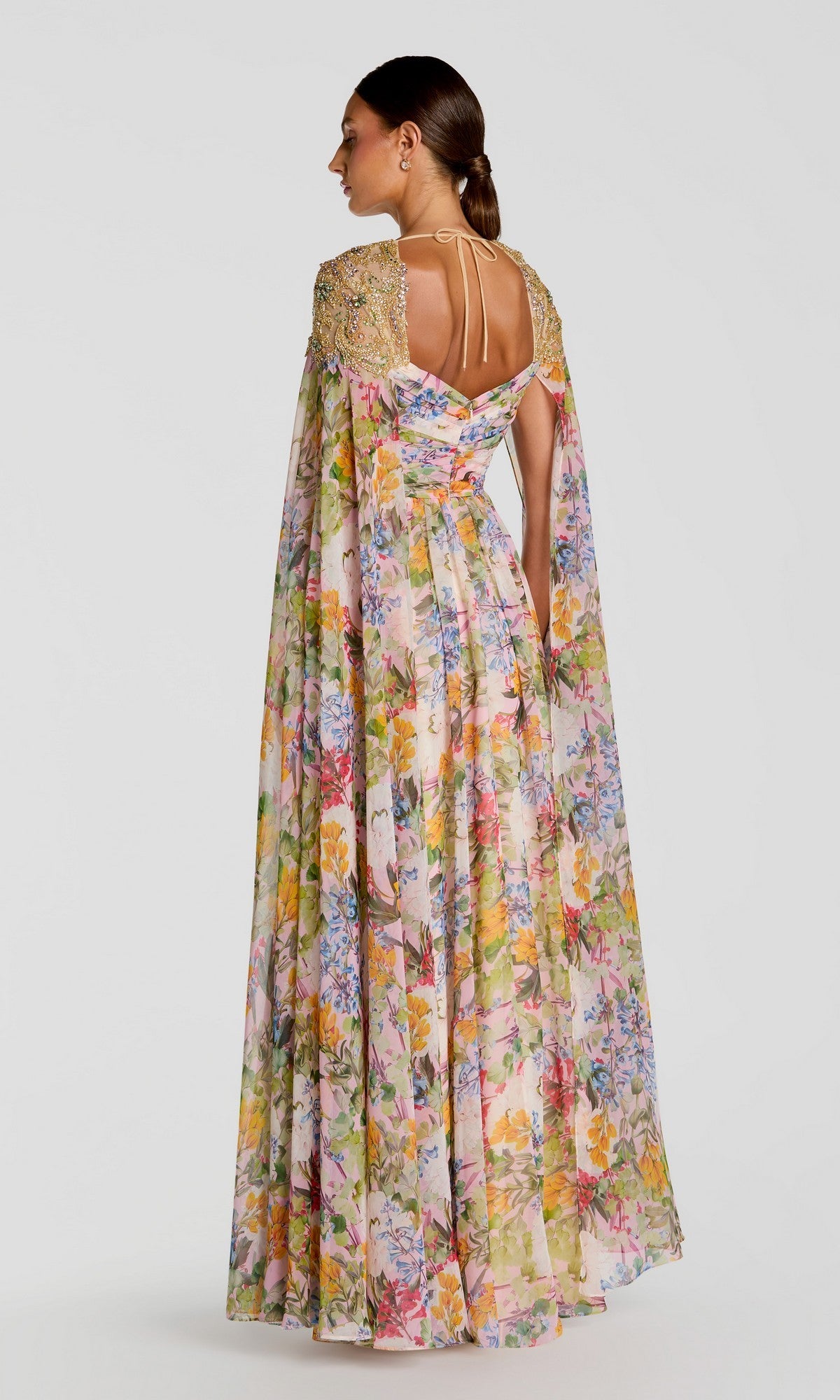 Woman turned away, wearing the Mac Duggal 11990 long formal dress—floor-length floral chiffon with gold-embellished shoulders, cape sleeves, and a keyhole back—ideal for special occasions.